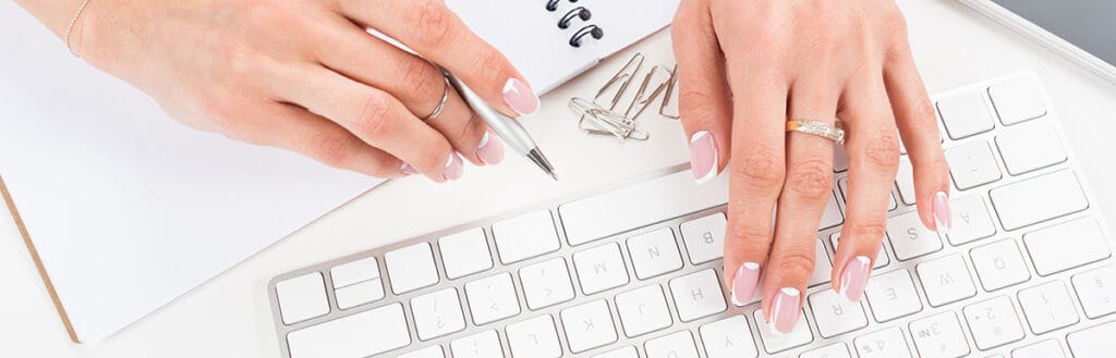 woman's hands on a keyboard with a pad of paper and pen.